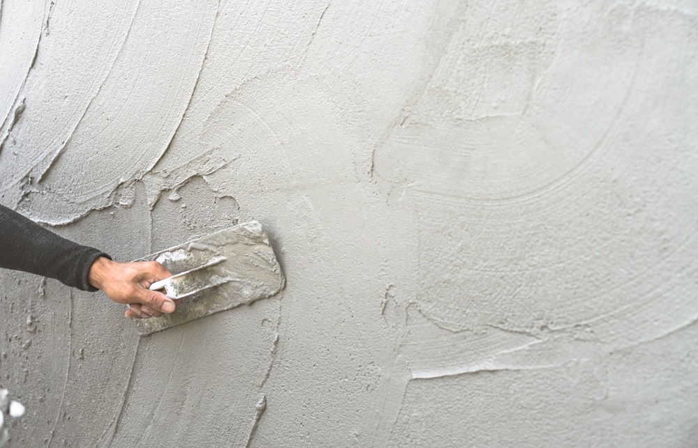 Enduit mural : application de crépi à la taloche Main d'un maçon appliquant de l'enduit de lissage au mur avec une taloche, révélant la texture du béton frais.