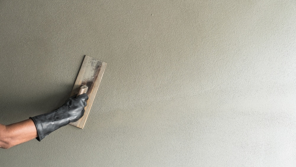 Application d'enduit de ciment à la truelle sur un mur Main gantée utilisant une truelle pour lisser un enduit de ciment gris sur un mur intérieur.
